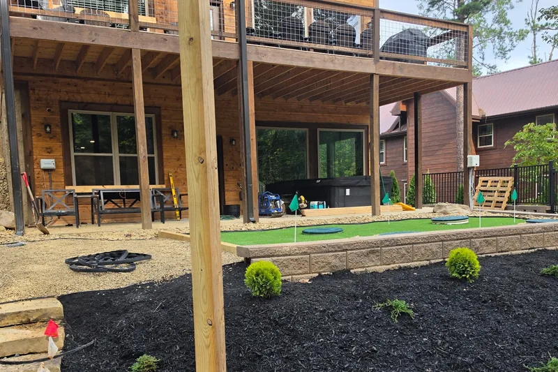 A back yard part-way through a staged build: finished retaining wall, putting green and planted beds in place while tools and gravel are still on site